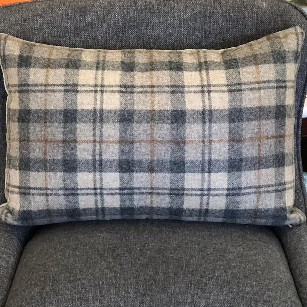 Pictured is Throw Pillow Wool Paid 14” x 20” by Honey Bee Fabrications sold at the gift shop The Hare & The Hart in downtown Thomasville, Georgia. It is a rectangular throw pillow covered in gray plaid fabric.