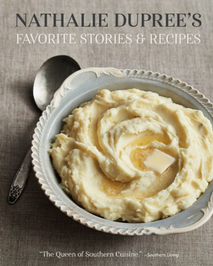 Pictured is the book "Nathalie Dupree's Favorite Stories & Recipes" by Nathalie Dupree sold at The Hare & The Hart in Thomasville, GA. On the cover is a picture of pureed mashed potatoes in a pretty dish. There is a pat of butter melting in the center of the swirl of mashed potatoes. There is a silver spoon sitting next to the bowl, ready to be eaten.