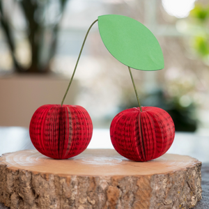 Pictured is a set of Paper Book Cherries sold at The Hare & The Hart in downtown Thomasville, Georgia. They are cherries made from book pages spread out, cut into the shape of cherries, and painted red, topped with green stems and a leaf.