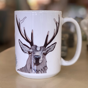 Pictured is a white coffee mug with a watercolor design of a hart on it. 