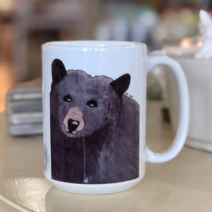 Pictured is a white coffee mug with a watercolor design of a black bear on it.