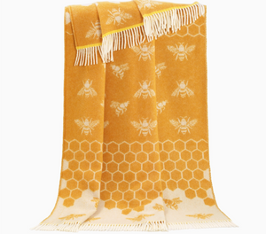 Pictured is a Bee Wool Throw by J. J. Textiles sold at The Hare & The Hart in downtown Thomasville, Georgia. It is a yellow and white wool blanket with bee and honeycomb designs. It has tassels.