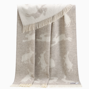 Pictured is a Hare Wool Throw by J. J. Textiles sold at The Hare & The Hart in downtown Thomasville, Georgia. It is a grey and white wool blanket with rabbit designs on it. It has tassels.