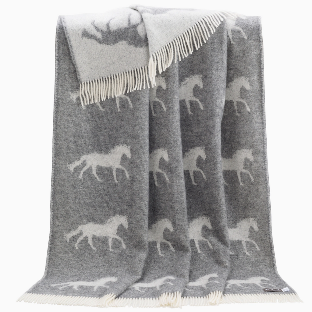 Pictured is a Horse Wool Throw by J. J. Textiles sold at The Hare & The Hart in downtown Thomasville, Georgia. It is a gray and white wool blanket with a horse design on it. It has tassels.