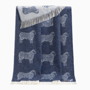Pictured is a Sheep Wool Throw in Blue sold at The Hare & The Hart in downtown Thomasville, Georgia. It is a blue and white wool blanket with a sheep design and tassels.