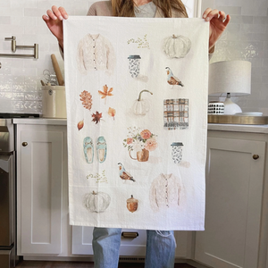 Pictured is a Autumn Tea Towel by Emily Lex sold at The Hare & The Hart in downtown Thomasville, Georgia. It is a tea towel with autumn related watercolor illustrations, like a sweater, a to-go coffee cup, a pumpkin, a quail, a plaid scarf, and a pair of slippers.