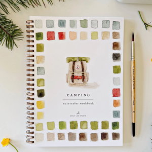 Pictured is a Camping Watercolor Workbook by Emily Lex sold at The Hare & The Hart in downtown Thomasville, Georgia. It has an illustration of a camping pack with watercolor paint swatches around it. The cover reads, "CAMPING watercolor workbook". It is surrounded by a paintbrush, a fir tree branch, and a flower.