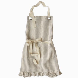 Pictured is Ruffle Pin Stripe Apron in Rust Stripe sold at The Hare & The Hart in downtown Thomasville, Georgia. It is a cotton and linen blend apron with a ruffle on the bottom and a tan striped pattern.