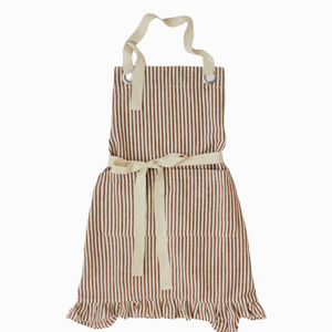 Pictured is Ruffle Pin Stripe Apron in Rust Stripe sold at The Hare & The Hart in downtown Thomasville, Georgia. It is a cotton and linen blend apron with a ruffle on the bottom and a red striped pattern.