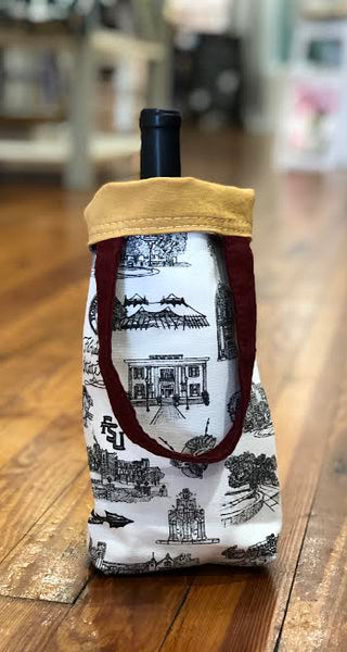 There is a Toile of FSU wine tote with a bottle of wine inside it pictured. The top edge of the wine tote is folded over, displaying the lining fabric which is gold.