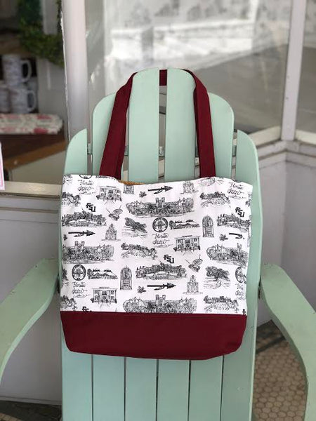 There is a tote bag hanging from the top of an adirondak chair. The tote is made of Toile of FSU fabric and has garnet accent fabric on the bottom and the straps.