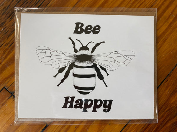 There is a horizontal notecard with a bee printed on it. The background is white and the design is black. There are the words "Bee Happy" printed around the bee. This is a Notecard by Birds & Bees sold at The Hare & The Hart.