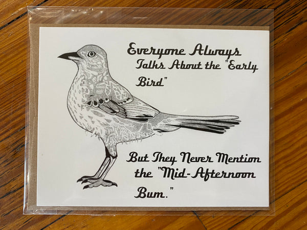 There is a horiztonal greeting card. It has a mocking bird drawing printed on it. The background is white and the design is black. There are the words "Everyone Always Talks About the 'Early Bird' But They Never Mention the 'Mid-Afternoon Bum'." printed on it. This is a Notecard by Birds & Bees sold at The Hare & The Hart.