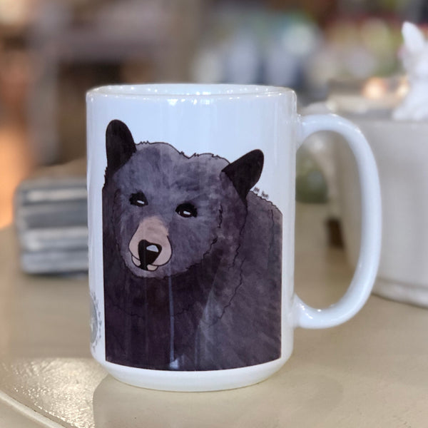 Pictured is a white coffe mug with a watercolor design of a black bear on it.