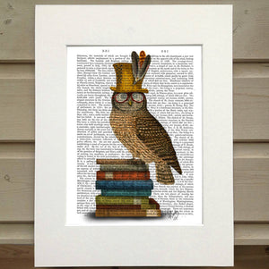 Pictured is a page from a book framed with mat. An opaque print of an owl is over the page. The owl is perched on a stack of books and it is wearing glasses and a gold feathered top hat.
