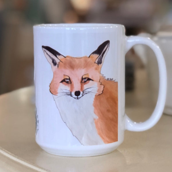 Pictured is a white coffe mug with a watercolor design of a fox on it.