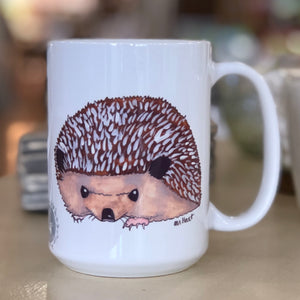 Pictured is a white coffe mug with a watercolor design of a hedgehog on it.