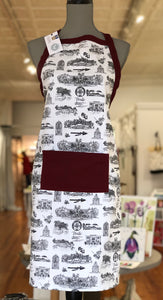 There is an apron on a mannequin. The apron is made with Toile of FSU fabric. There is a wide pocket on the front at about waist height and a trim around the top edge of the apron and both are made of garnet fabric.