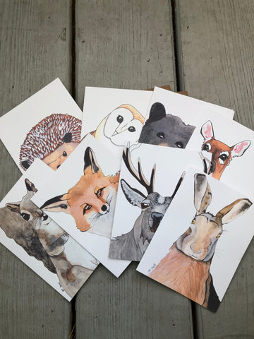 There are eight notecards splayed out. Each notecard has a different animal design on it. The designs are: squirrel, hedgehog, fox, owl, bear, deer, doe, and hare.