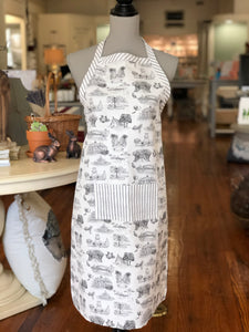 Pictured is an apron on a mannequin. The apron is made of black and white Toile of Tallahassee fabric in small print. There is a pocket in the center front of the apron and it is made of black and white ticking stripe fabric. The border of the top edge of the apron and the neck strap are also made of the black and white ticking stripe fabric.