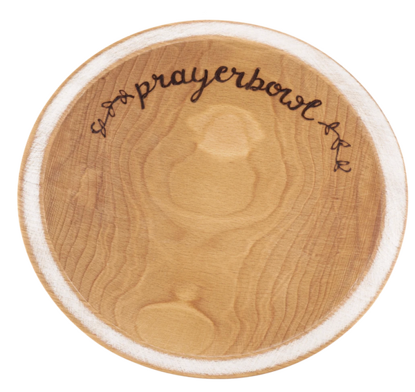 Pictured is the Grace Prayer Bowl. It is carved out of wood and has a natural finish. The lip of the bowl is wide and painted white. Carved into the bowl along one edge, in cursive, is the words "prayerbowl" and two flower designs on either side.