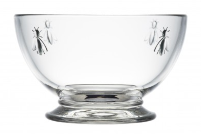A clear glass bowl with four bee designs embossed on opposite ends from one another is pictured. This is a Bee Bowl by La Rochere sold by The Hare & The Hart.