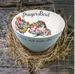 The Josephine Prayer Bowl is pictured from the side, so the painting inside is visible. The bowl is round and deep. Inside, it is painted white with the deisgn on a bird made of flowers perched on a limb taking up one wall of the bowl. Above the bird, in cursive script, are the words "Prayer Bowl." The outside of the bowl is light blue wth a border of cursive script.
