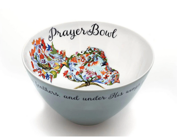 The Josephine Prayer Bowl is pictured from the side, so the painting inside is visible. The bowl is round and deep. Inside, it is painted white with the deisgn on a bird made of flowers perched on a limb taking up one wall of the bowl. Above the bird, in cursive script, are the words "Prayer Bowl." The outside of the bowl is light blue wth a border of cursive script.