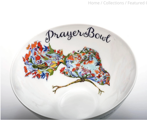 This is a close up of the design on the inside of the Josephine Prayer Bowl. It is of a bird perched on a thin branch. The bird is made up of a light blue background with plants and flowers over top. It has a visible eye and beak. Above the bird are the words "Prayer Bowl" in cursive script.