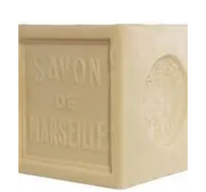 Pictured is a block of palm oil soap by Savon de Marseille. Etched into the side of it is the name of the brand. It is cream in color.