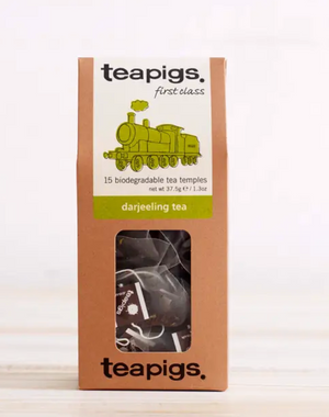 Pictured is the packaging for Teapigs Darjeeling Tea. It is a tall brown box with a clear plastic window showing the teabags. The label is white with a green steam engine design. The label reads "teapigs first class 15 biodegradable tea temples darjeeling tea."