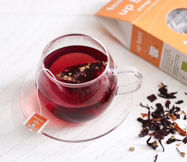Pictured is a cup of tea next to loose leaf tea and a package of teapigs organic upbeet tea.