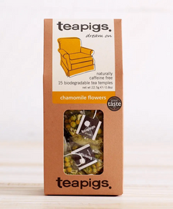 Pictured are the Teapigs Chamomile Flowers in their packaging. The pacakging is a brown box with a little clear window in the center, through which the teabags are visible. On the packaging is a white and yellow label with an image of a comfy armchair. The label reads "teapigs dream on," "naturally caffeine free 15 biodegradable tea temples," "chamomile flowers."