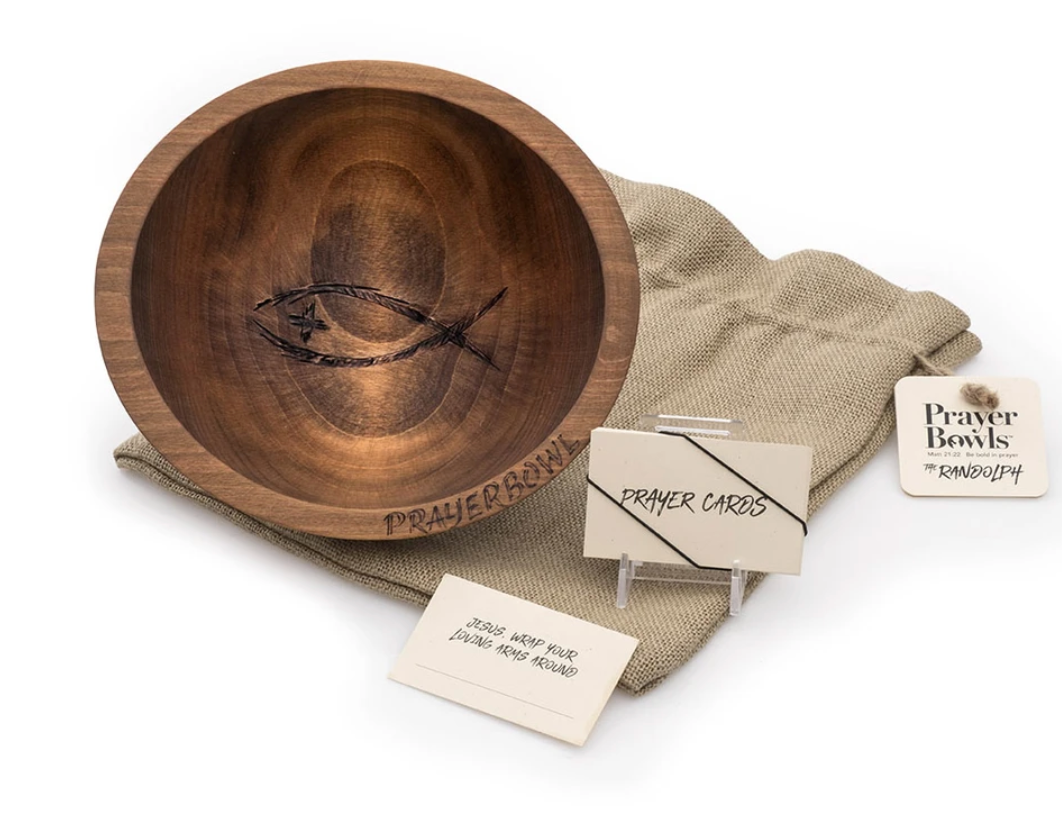 Pictured is the Randolph Prayer Bowl sitting on top of its burlap sack packaging, next to a stack of prayer cards that come with it.