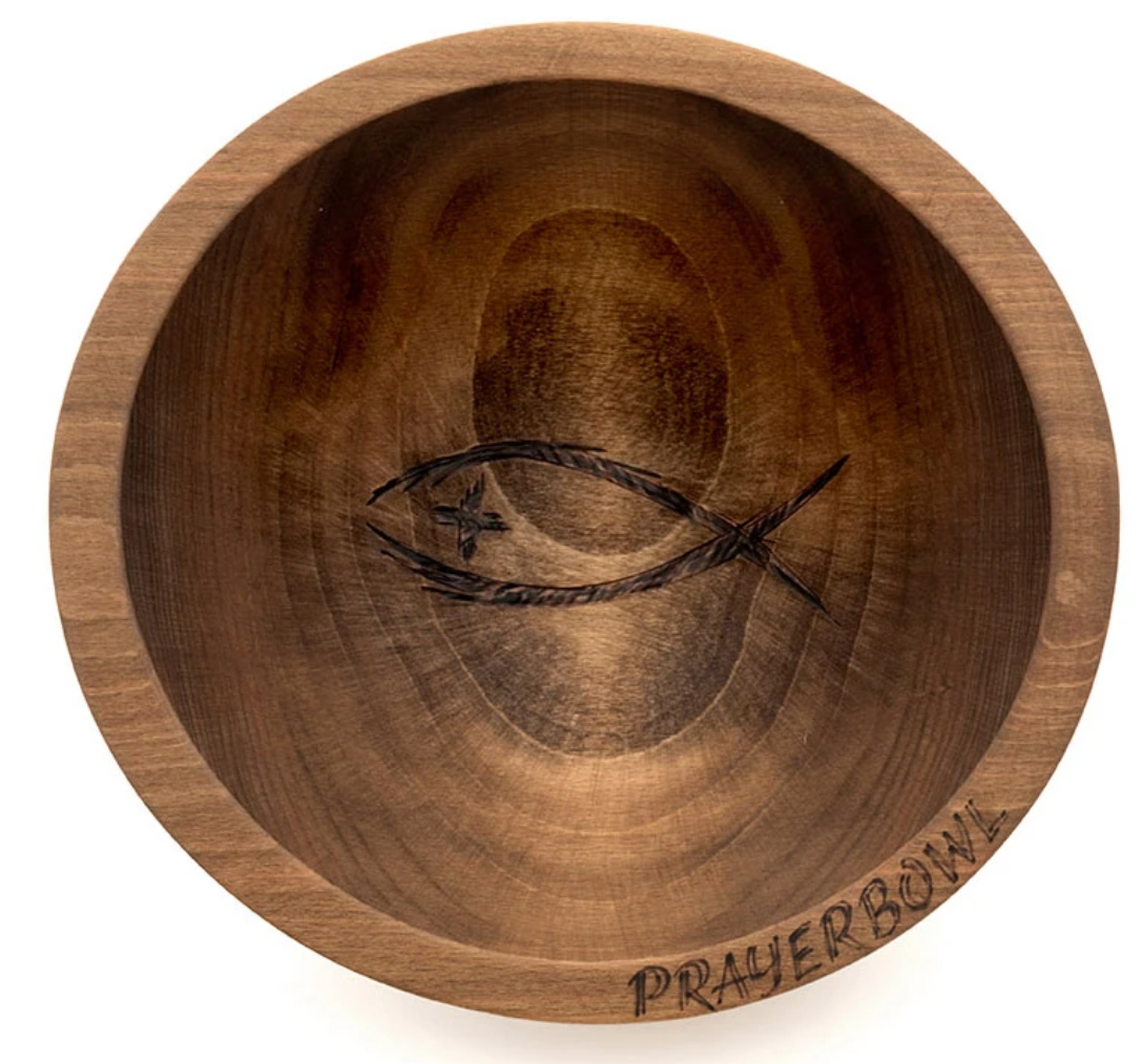 Pictured is the Randolph Prayer Bowl. It is a simple, shallow bowl carved from wood. In the center is a carving of an ichthys with a cross for an eye. On the bottom edge of the bowl is a carving of the words "PRAYER BOWL"