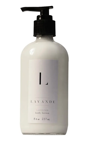 Pictured is a glass lotion dispenser with a pump top lid. It is filled with lotion and it has a white label on it that reads "L LAVANDE LAVENDER body lotion"