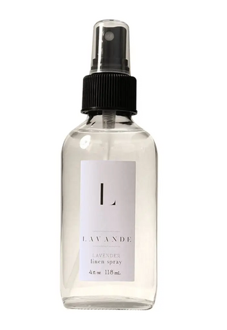 Pictured is a glass spray bottle of Lavande Linen Spray. The liquid inside is clear. The bottle has a white Lavande label sticker on it.