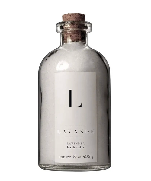 It is a glass bottle with a cork in the top. It is filled with lavender bath salts. The bottle has a white label that reads "L LAVANDE LAVENDER bath salts"