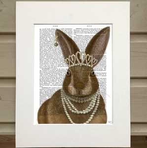 There is a page from a book framed with mat. Printed over the words on the page is the image of a bunny wearing several pearl necklaces, a crown of pearls, and an earring with a bell in one ear.