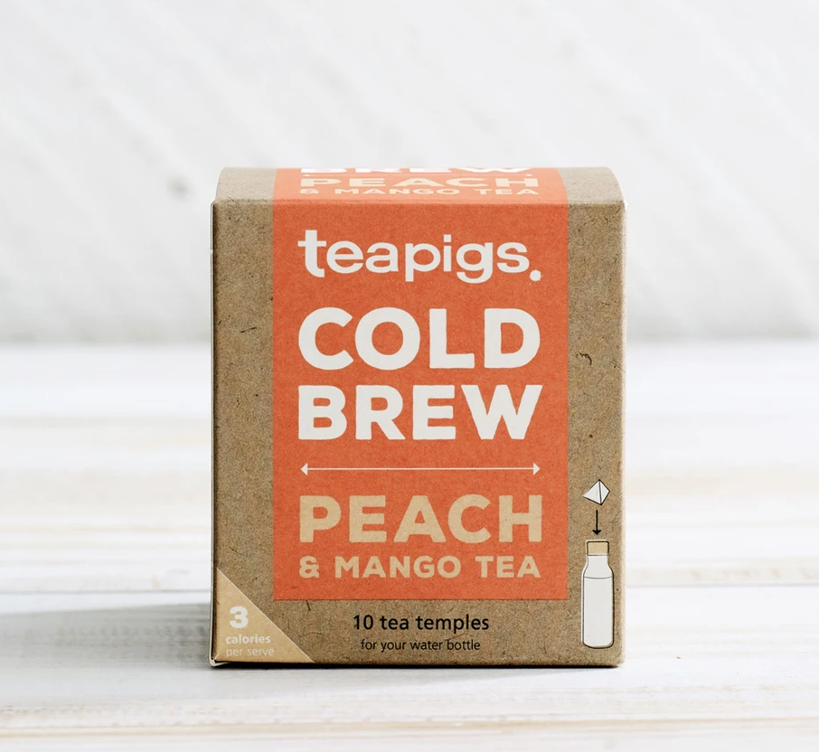 There is a brown square package of Teapigs Cold Brew Peach and Mango tea. The orange label on it reads "teapigs COLD BREW PEACH & MANGO TEA," "10 tea temples for your water bottle," "3 calories per serving."