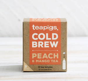There is a brown square package of Teapigs Cold Brew Peach and Mango tea. The orange label on it reads "teapigs COLD BREW PEACH & MANGO TEA," "10 tea temples for your water bottle," "3 calories per serving."