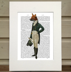 This is a Dressed Up Fox Book Print by FabFunky Ltd. sold at The Hare & The Hart. There is a pag from a book surrounded by mat. Printed on top of the words on the page is an image of a fox with a man's body. The fox is wearing traditional English clothing and is holding a tophat and cane in its hand.