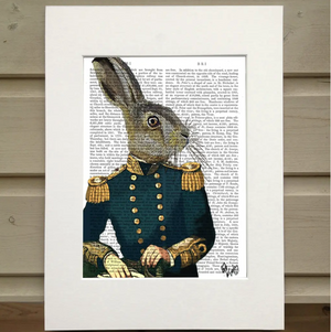 There is a page out of a book framed in mat. Printed over the page is a figure visible from the waist up. It wears a blue military uniform with gold buttons and accents. Instead of having the head of a man, the figure has the heads of a hare.