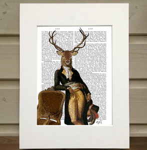 There is a print framed in a mat. The print is of a page from a book with an image over it. The image is of a figure wearing old fashioned clothes and leaning on a velvet chair. The figure has the head of deer with antlers rather than the head of a man. This is an Animal Book Print by FabFunky Ltd. sold at The Hare & The Hart.