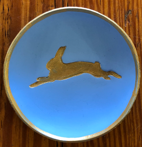 Pictured is a light blue blessing bowl with a gold leaping hare in the center of it. The rim of the clay bowl is also gold. Made in Oxford, MS by artist Carrie Cox and sold at The Hare & The Hart.