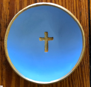 Pictured is a light blue blessing bowl with a small, gold cross in the center of it. The rim of the clay bowl is also gold. Made in Oxford, MS by artist Carrie Cox and sold at The Hare & The Hart.