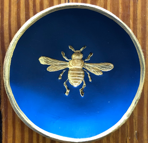 Pictured is a dark blue blessing bowl with a gold bee in the center of it. The rim of the clay bowl is also gold. Made in Oxford, MS by artist Carrie Cox and sold at The Hare & The Hart.