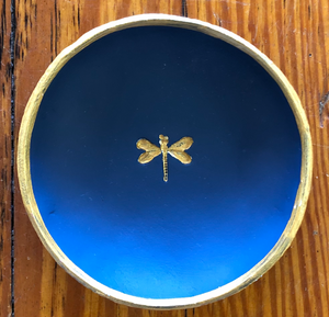Pictured is a dark blue blessing bowl with a small, gold dragonfly in the center of it. The rim of the clay bowl is also gold. Made in Oxford, MS by artist Carrie Cox and sold at The Hare & The Hart.