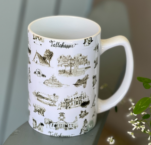 There is an average sized ceramic coffee mug. The mug has a white background and black Toile of Tallahassee design.