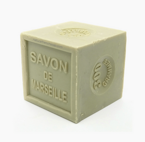 Pictured is an olive oil soap block by Savon de Marseille. The block is cut into a cube and is stamped with SAVON DE MARSEILLE.